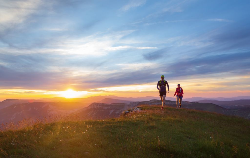 two people running at sunrise atop a hill in the wilderness