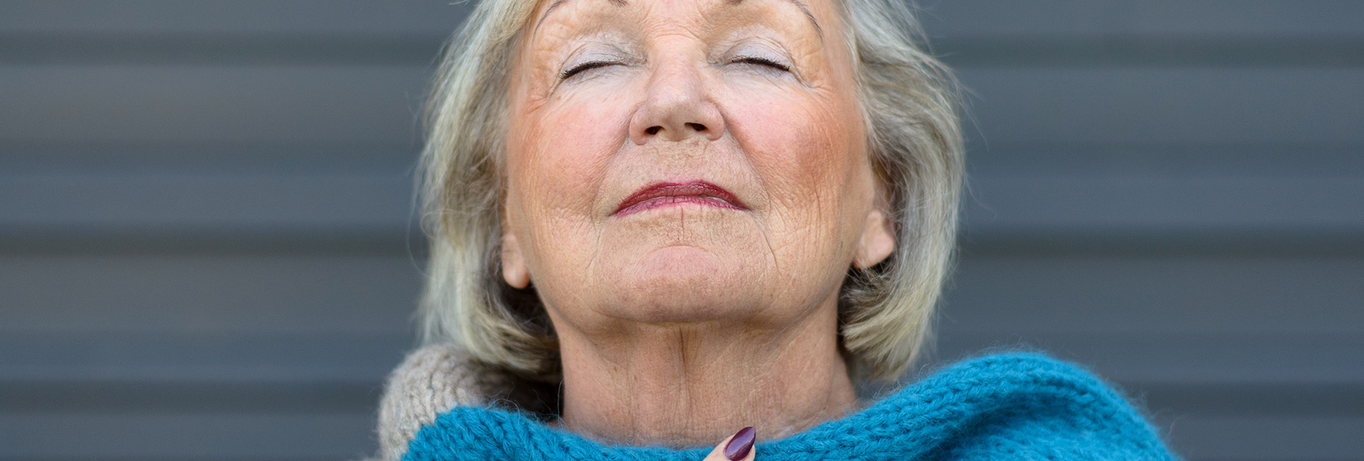 An older woman closing her eyes and taking a cleansing breath