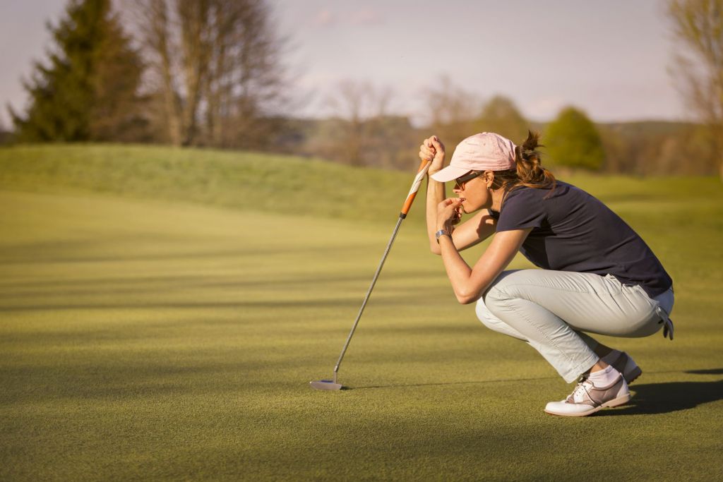 a woman squats down to assess her next golf shot