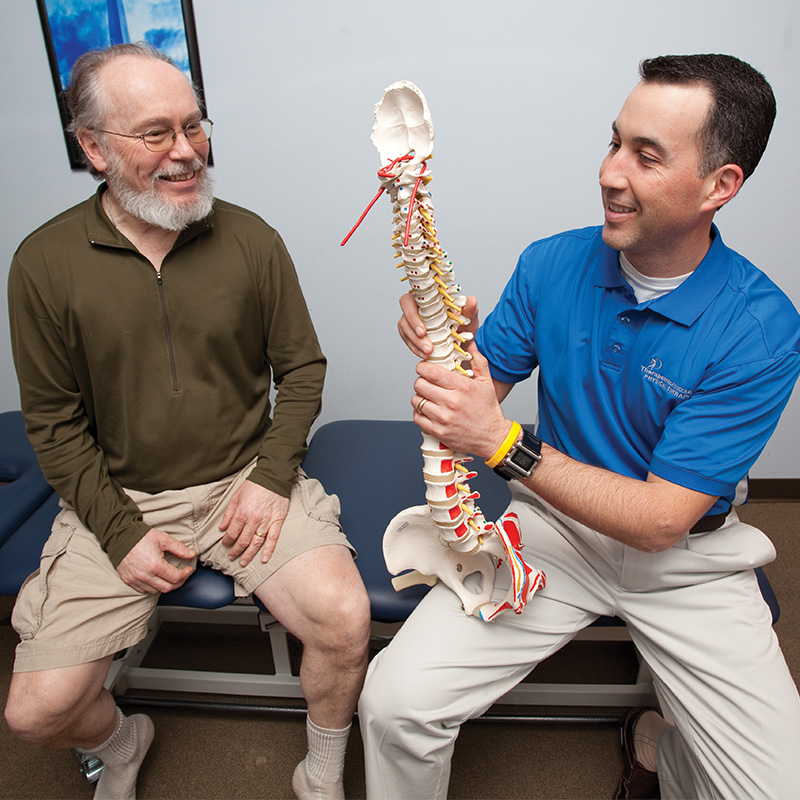 A PT uses a prop of a spine to explain an injury to a patient