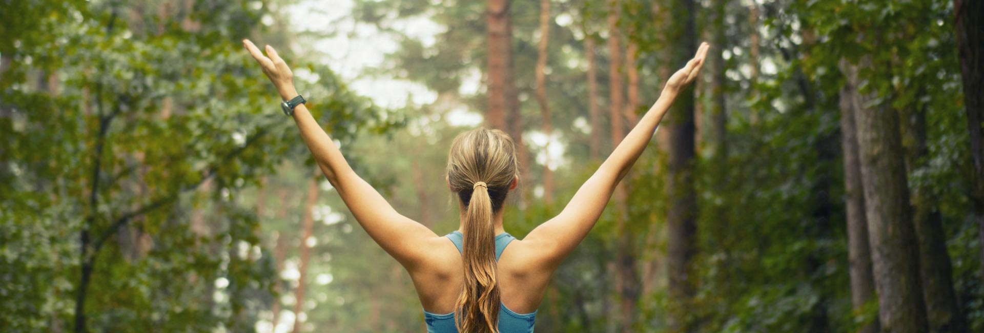 a woman holds her arms up in a wide "Y" outdoors - breathing