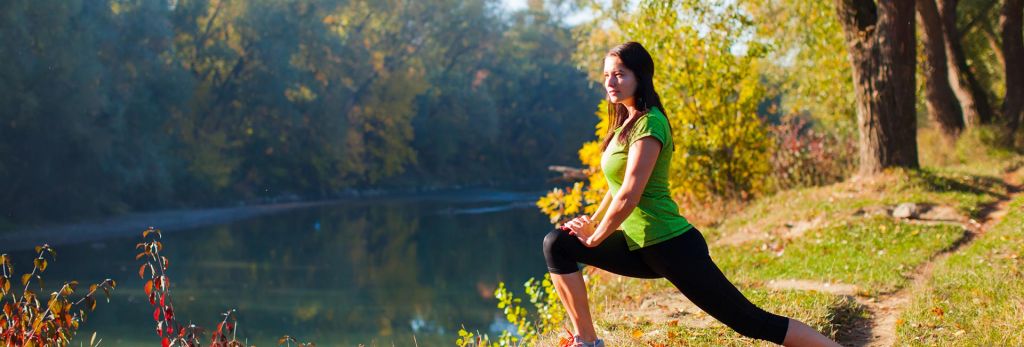 a woman lunges next to a river - stretching