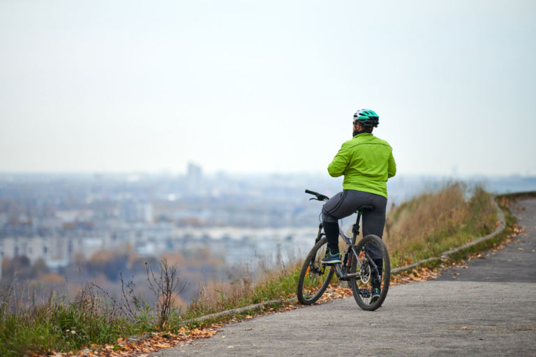 Cyclist on top of hill looking at cityscape, back view.