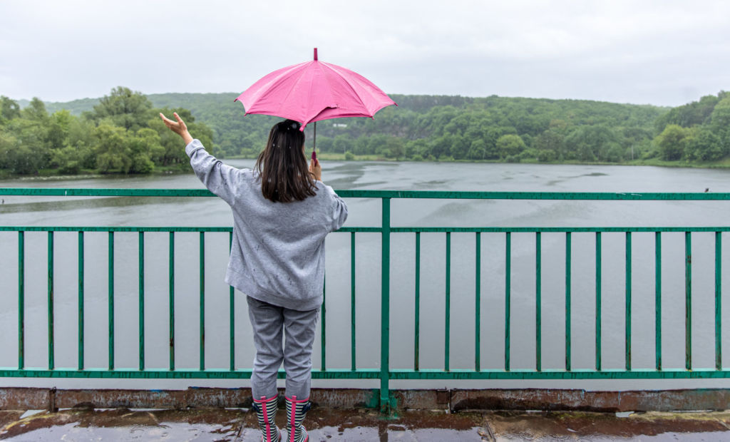 A young woman takes a moment to take in the view of the river holding a pink umbrella