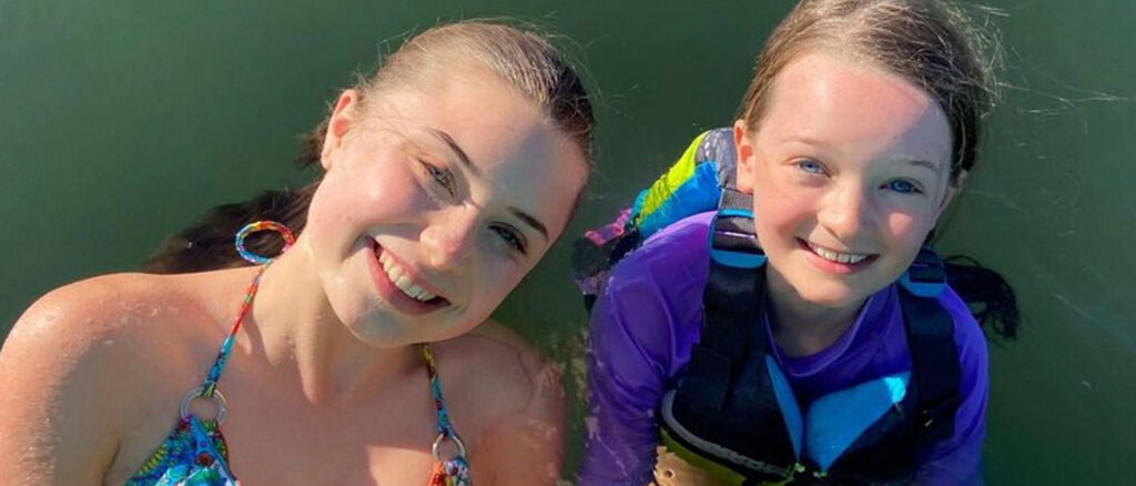 Teen girl and younger sister smile to camera during a fun swimming adventure.