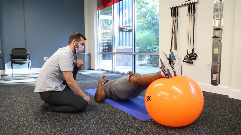 physical therapist guides patient on floor exercise with yoga ball