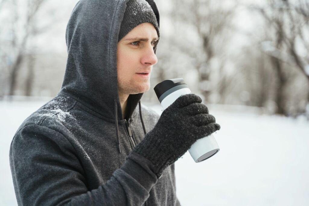 man drinks from thermal water bottle during snowy cold-weather workout