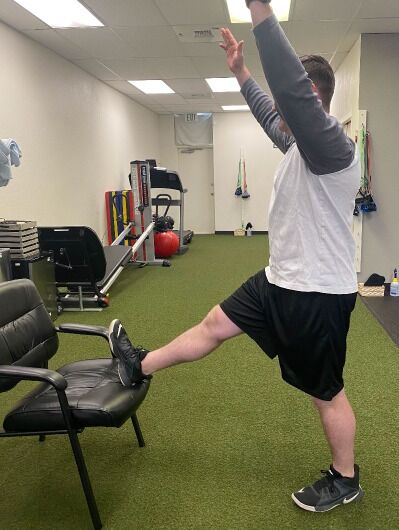 demonstrating standing hamstring stretch with chair and overhead reach