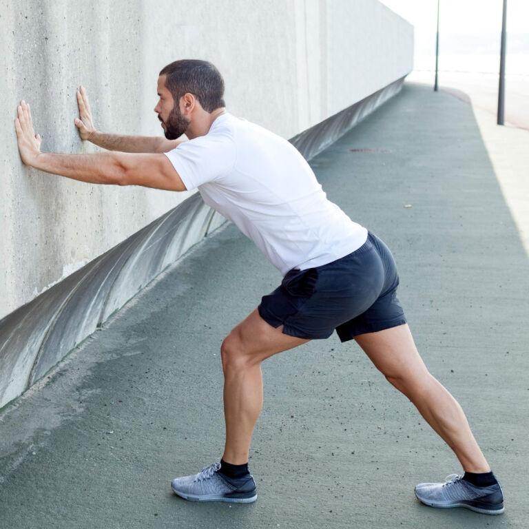 man stretches by leaning into a wall