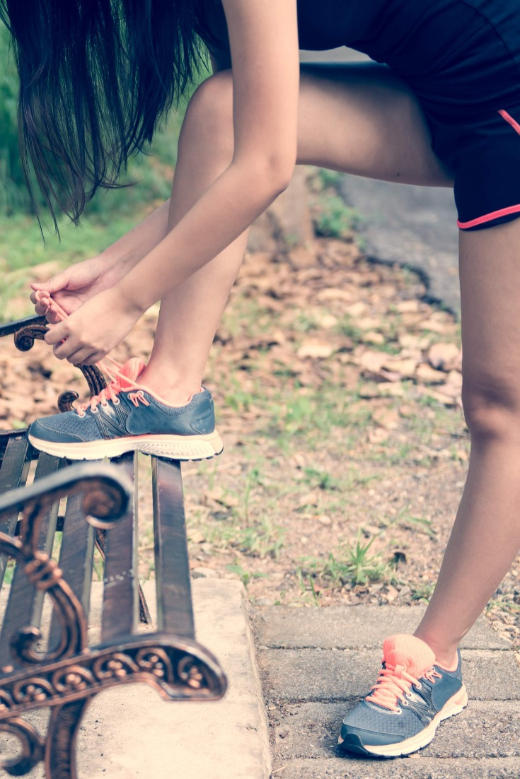 woman ties her shoe on a park bench while out for a walk