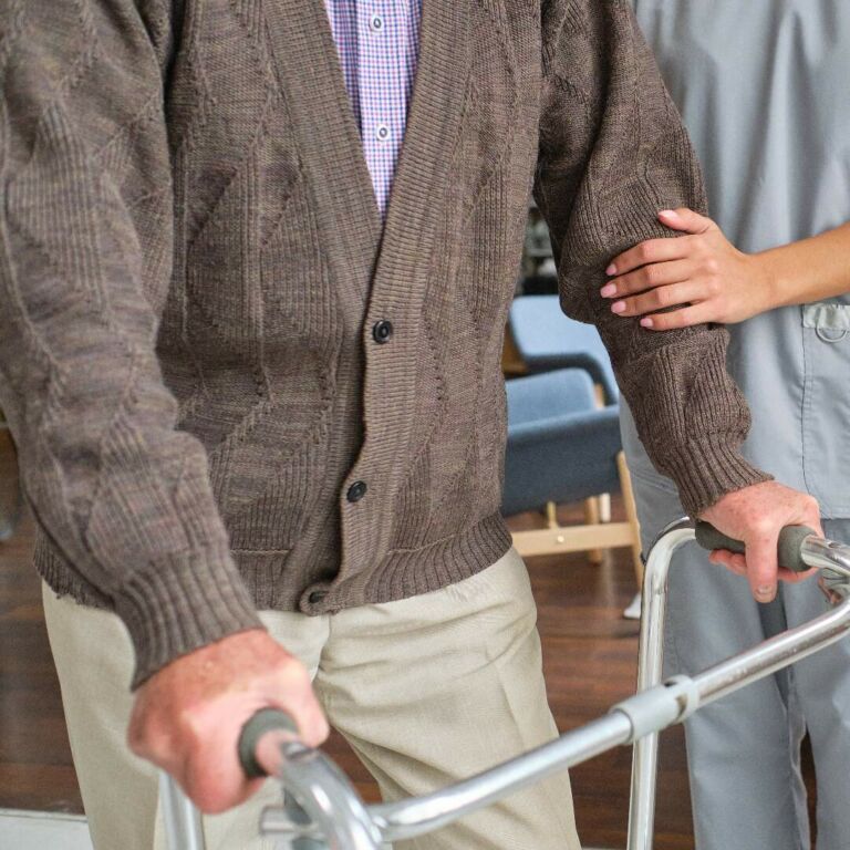 physical therapist assists an elderly man learning to use a walker
