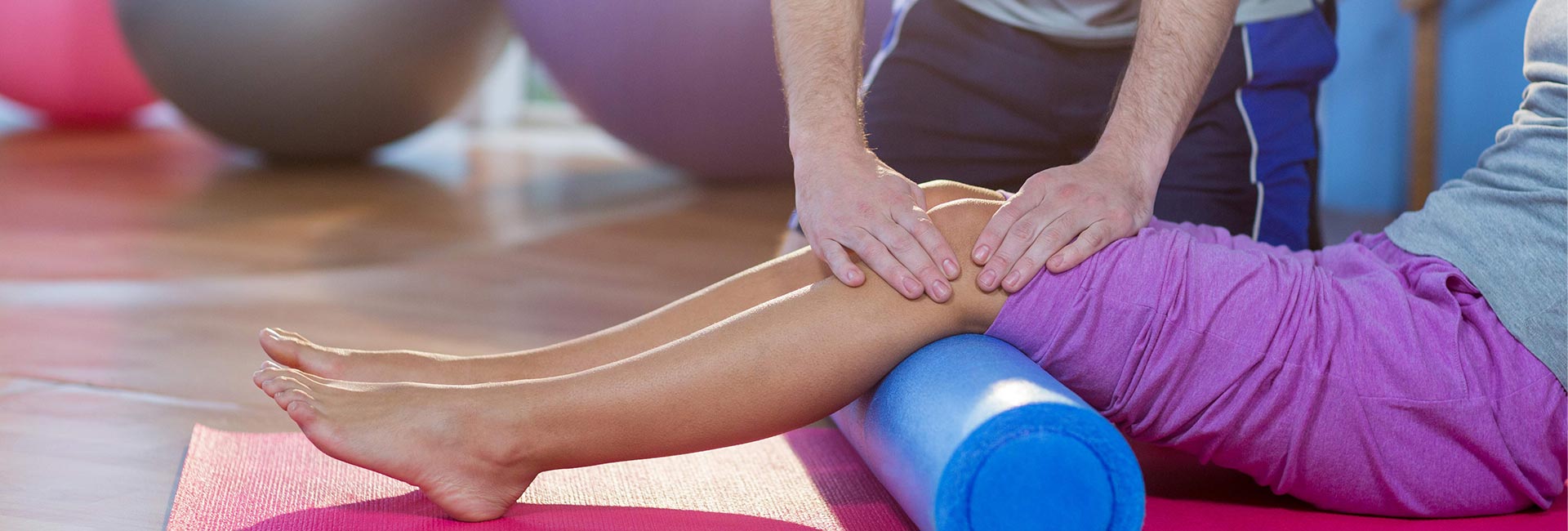 a PT assists with foam rolling while utilizing manual therapy on a patient's legs
