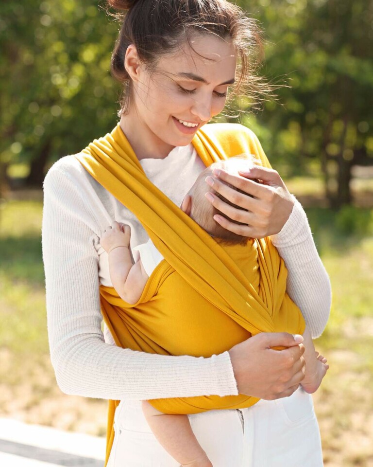 A woman looks lovingly at her baby in a front wrap while out on a walk in nature