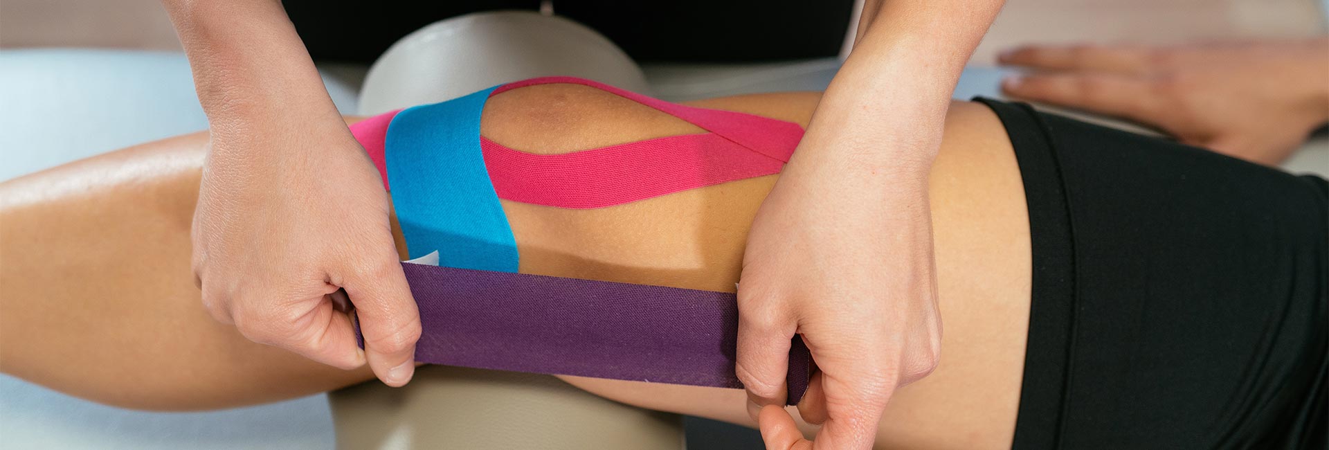 A physical therapist applies KT tape to a patient's knee