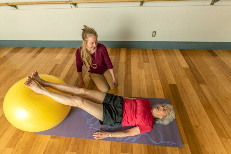 An older woman works with a physical therapist using an exercise ball