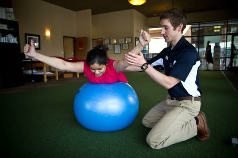a physical therapist works with a patient on back and shoulder mobility and flexibility using an exercise ball