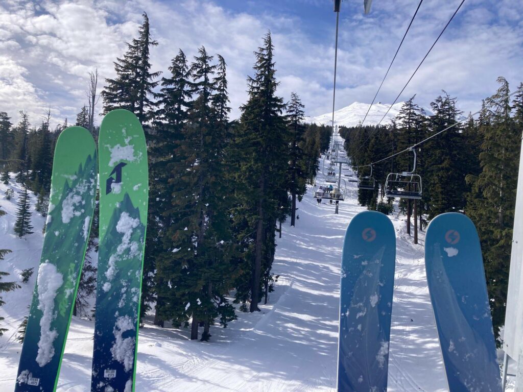 skiers hold their skis up in front of them as they ride up the chair lift at Mount Bachelor