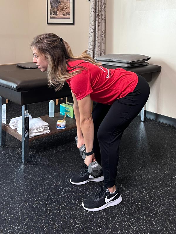 demonstration of a hinge or deadlift exercise using dumbbells