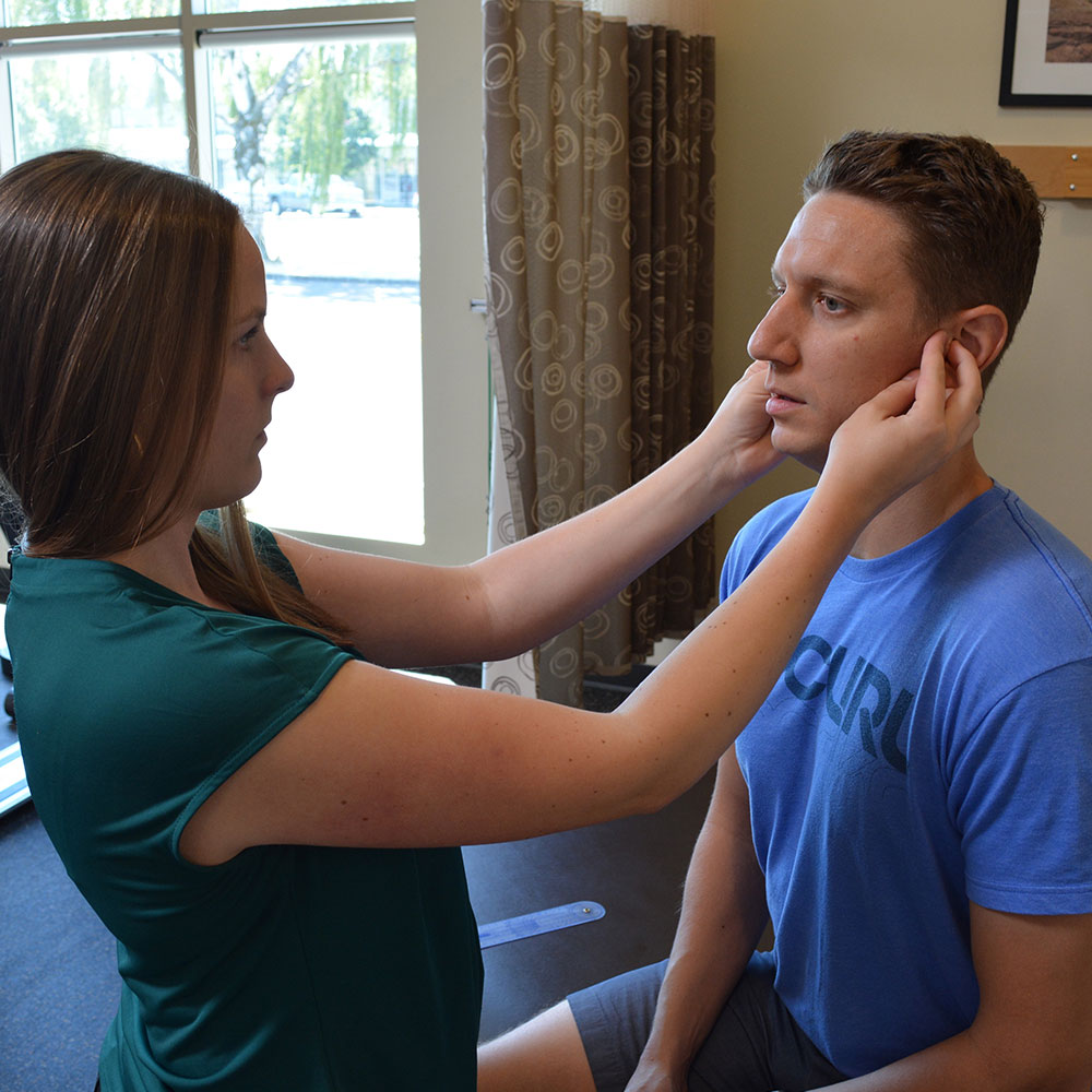 A PT checks a patient's ears during myofunctional therapy for TMJ