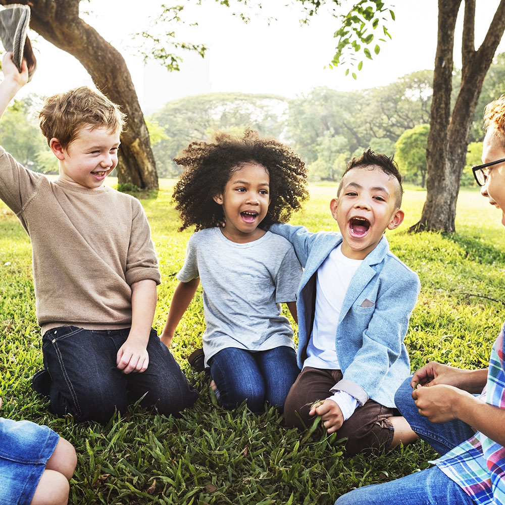 a group of young children smile and laugh while sitting outside in the grass