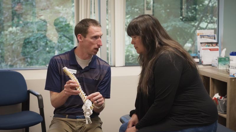 physical therapist shows a paitent what may be her cause of pain using a model of the spine