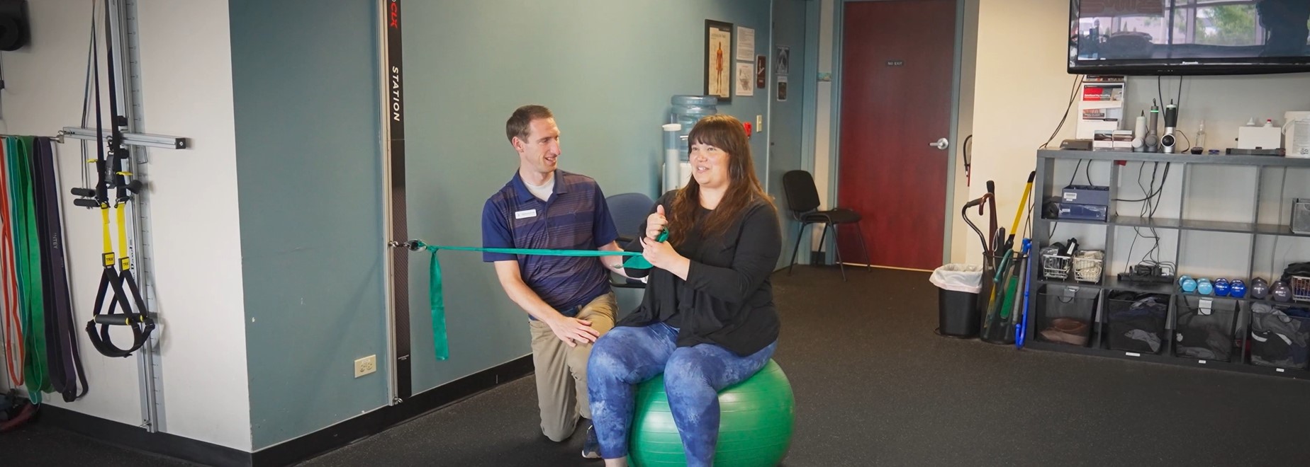 physical therapist assist a woman with exercise while using a yoga ball