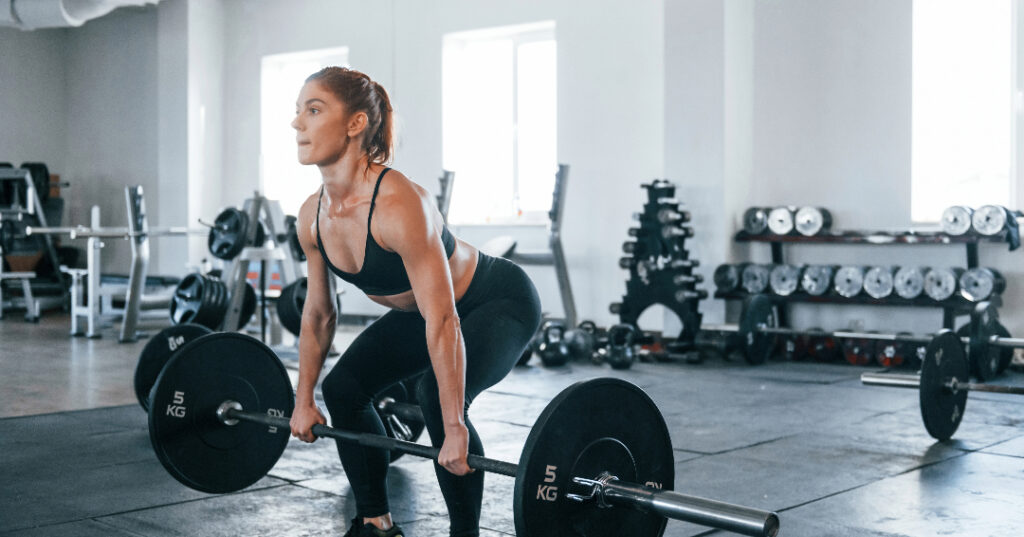 a young woman trains for CrossFit athletics by weight lifting doing a deadlift exercise