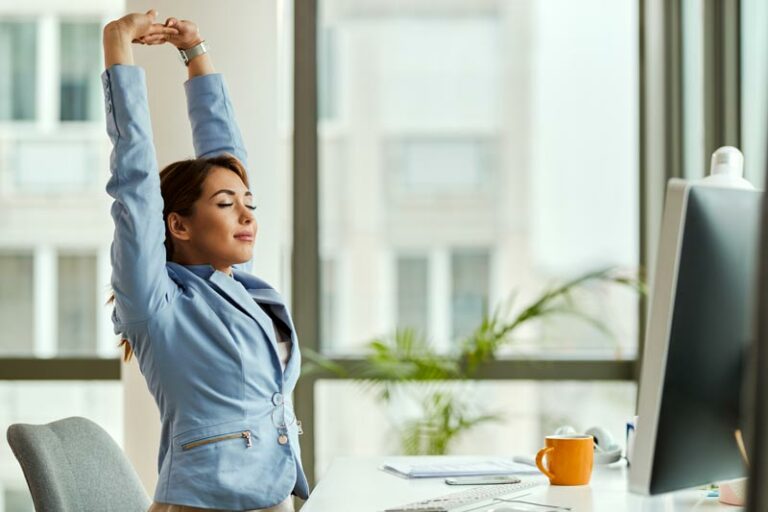 a woman stretches her arms overhead while sitting at her desk job for ergonomic reset