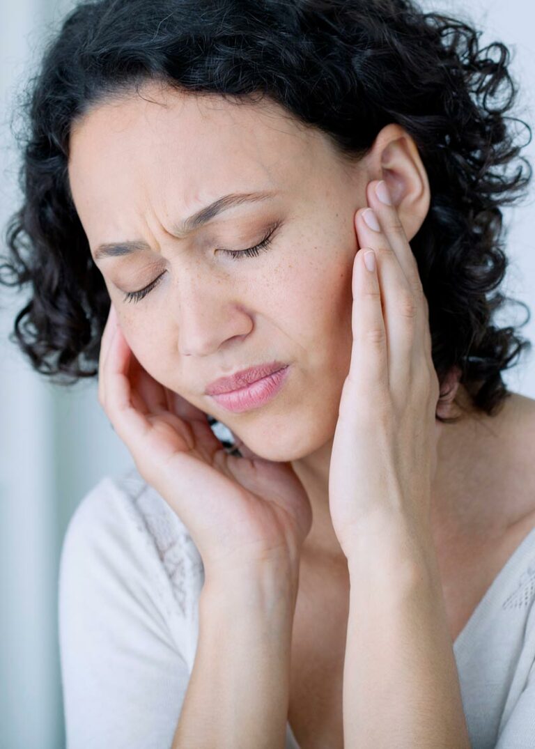 a woman holds her ears next to her jaw in pain