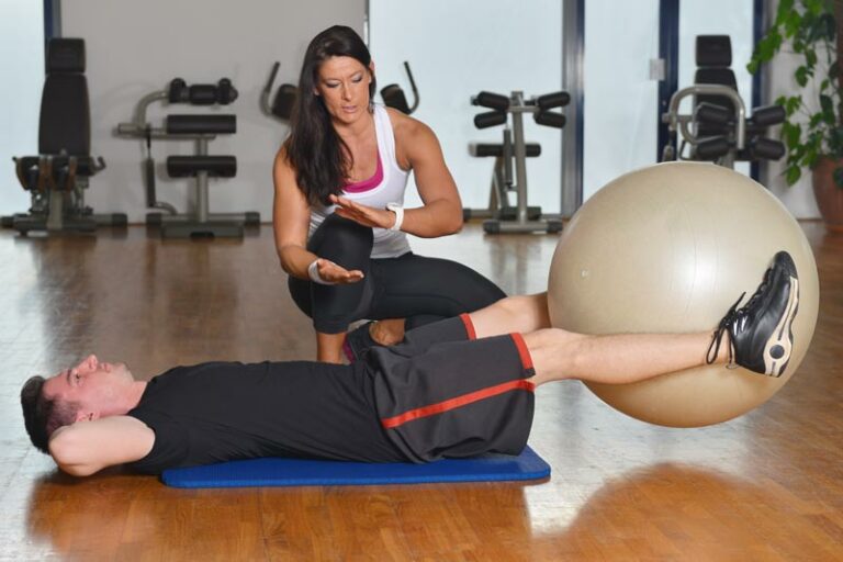 physical therapist assists male patient with exercise for core and pelvic floor utilizing a yoga ball