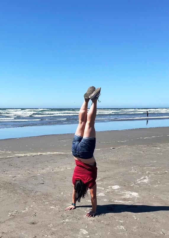 a young woman does a handstand on the sand at the beach