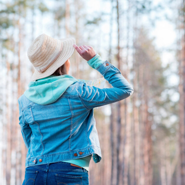 rear view of a woman holding the brim of her hat while on a walk in the forest in nature