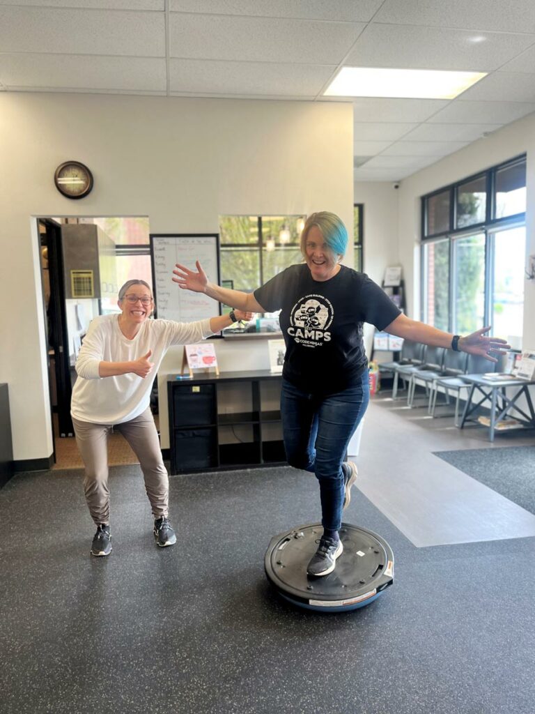 balancing on a stability ball at Hillsboro physical therapy, ankle rehab patient Cindy Davidson celebrates success alongside her PT Bailey Ouellette