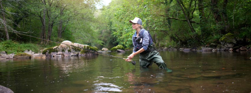 A woman wades into the river in pursuit of catching a fish on her fly rod