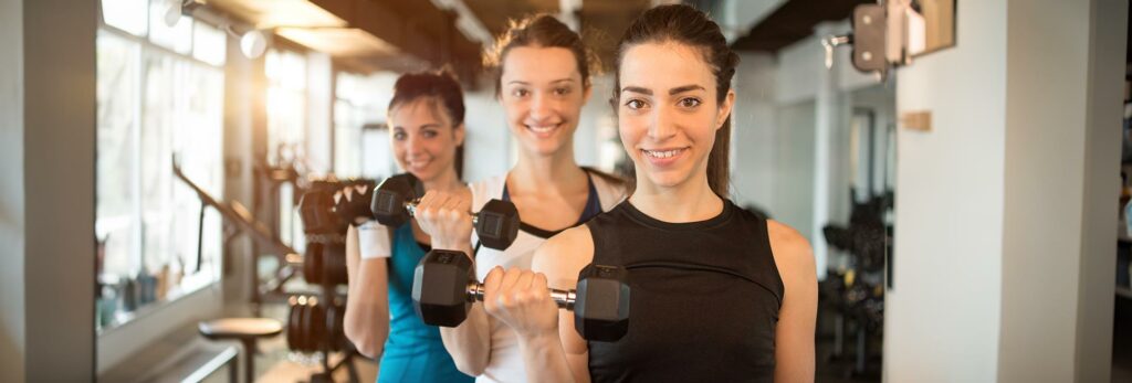 teenage girls hold their dumbbells and smile during a workout lifting weights