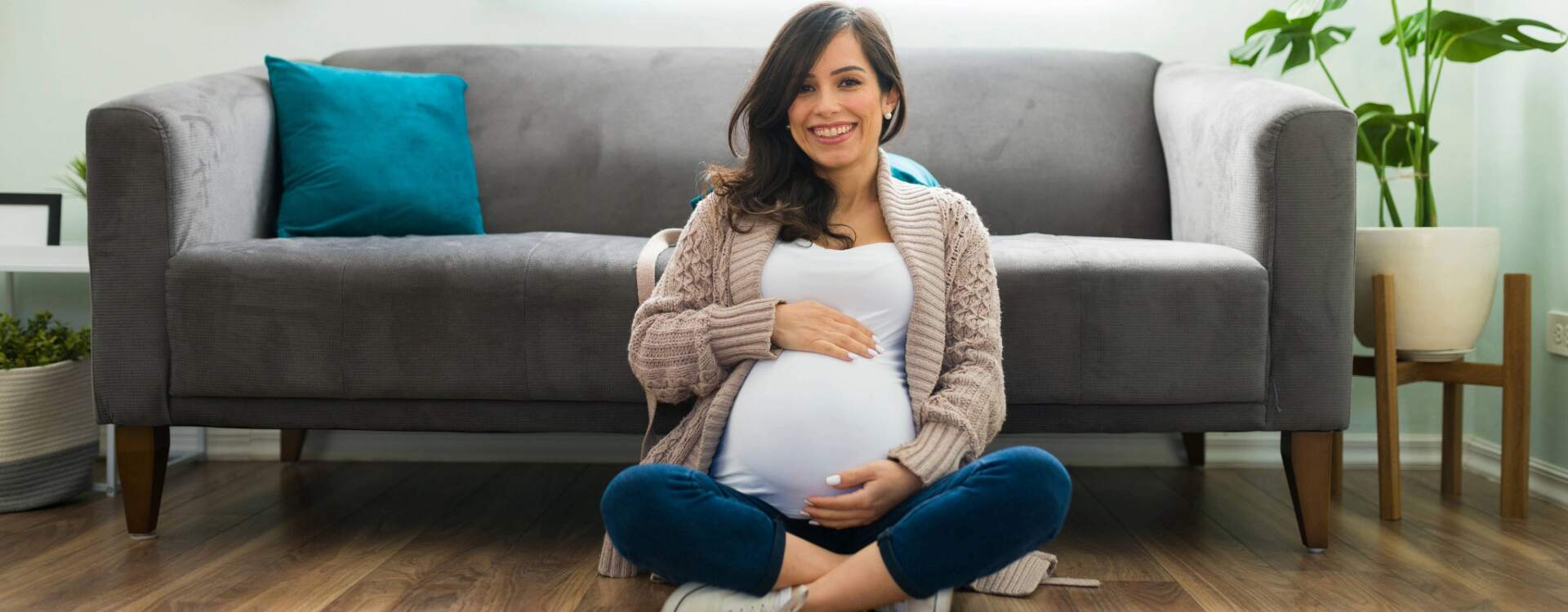 pregnant woman sitting crisscross on floor smiling and holding baby belly