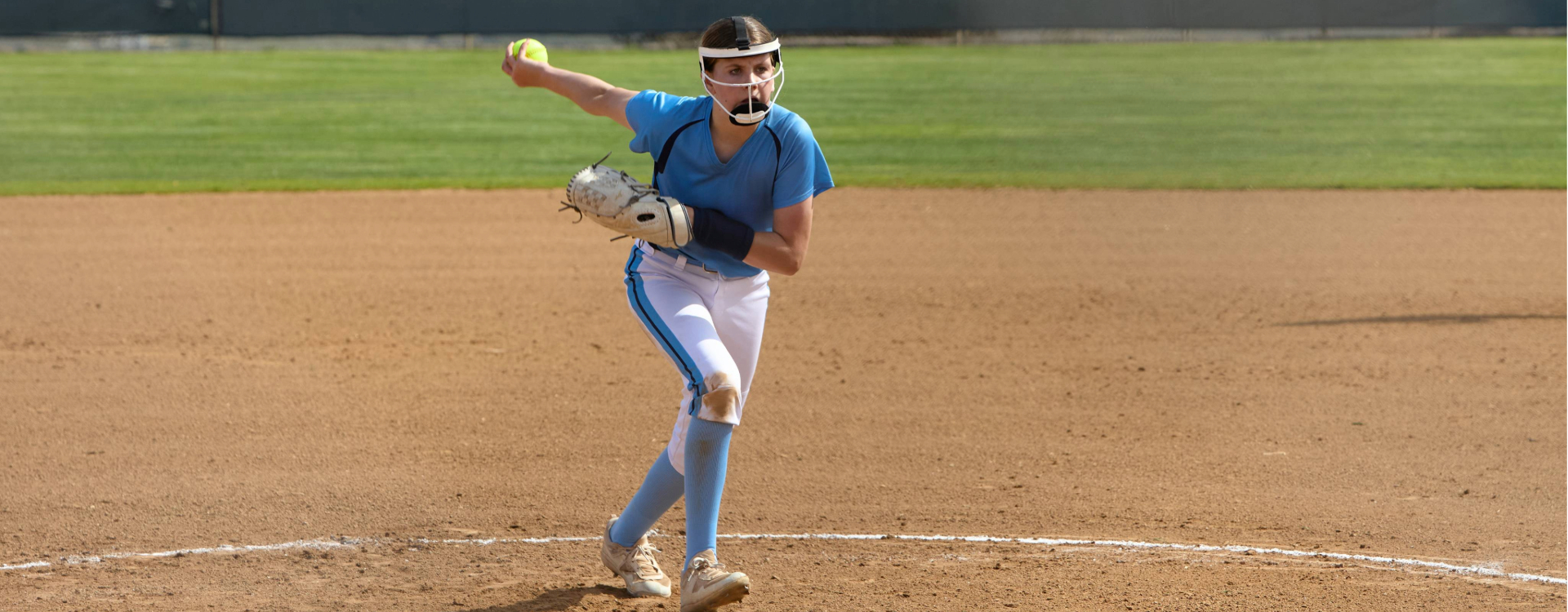Youth athletics - a fastpitch softball pitcher throws a windmill, or underhand, pitch from the pitcher's mound during a game.